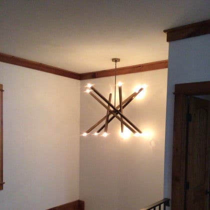 Unique modern chandelier with wooden branches and warm lights in a cozy interior setting.