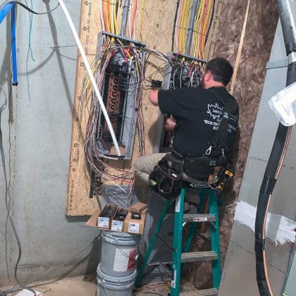Electrician working on wiring installation in a basement, using a step ladder and tools.