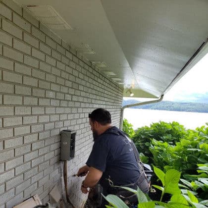 Technician working on exterior wall with ventilation systems near water.
