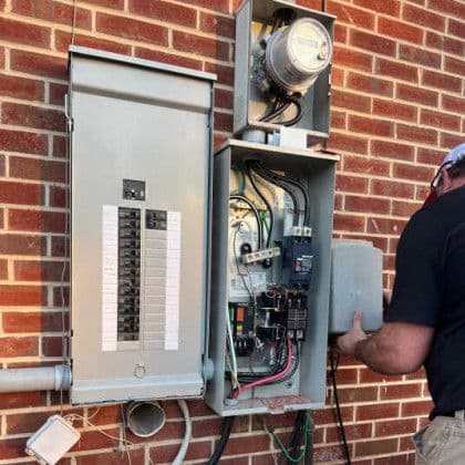 Electrician servicing electrical panel and meter on brick wall, ensuring proper maintenance.