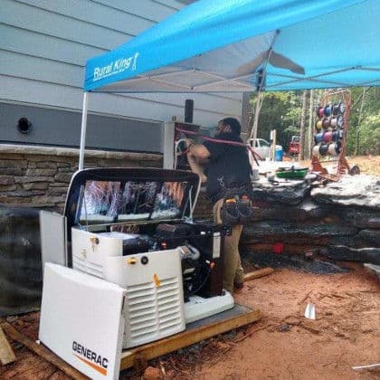 Man installs a Generac generator under a tent at a construction site. Rural King branding visible.