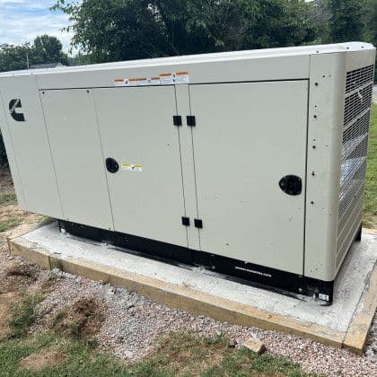 Cummins generator on a concrete base in a landscaped outdoor setting.