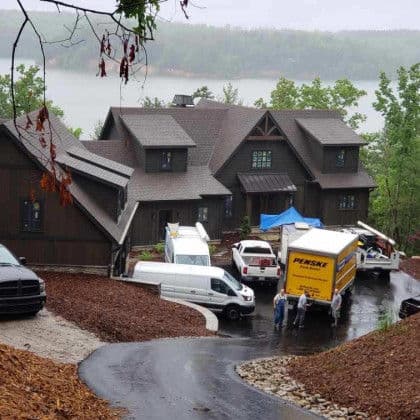 Newly built house on hillside with moving trucks and workers during rainy weather.