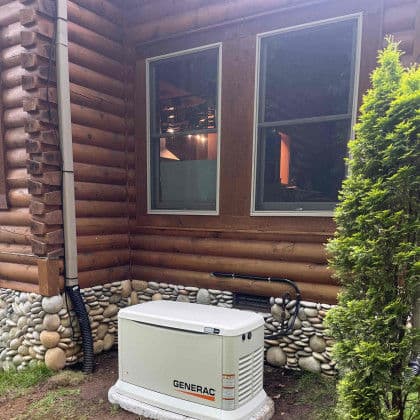 Generac generator installed outside a log cabin near windows and decorative stonework.