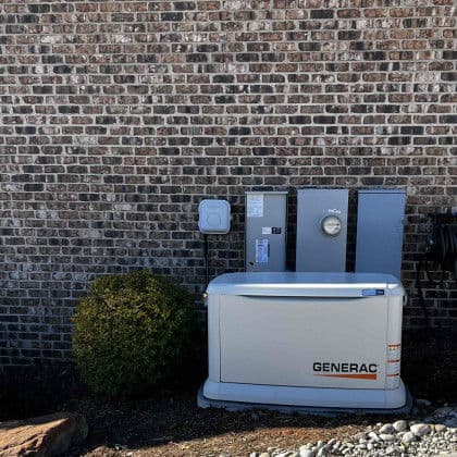 Generac home generator installation against a brick wall with utility connections.