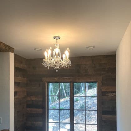 Chandelier with clear crystals hanging in a room with wood-paneled walls and a large window.