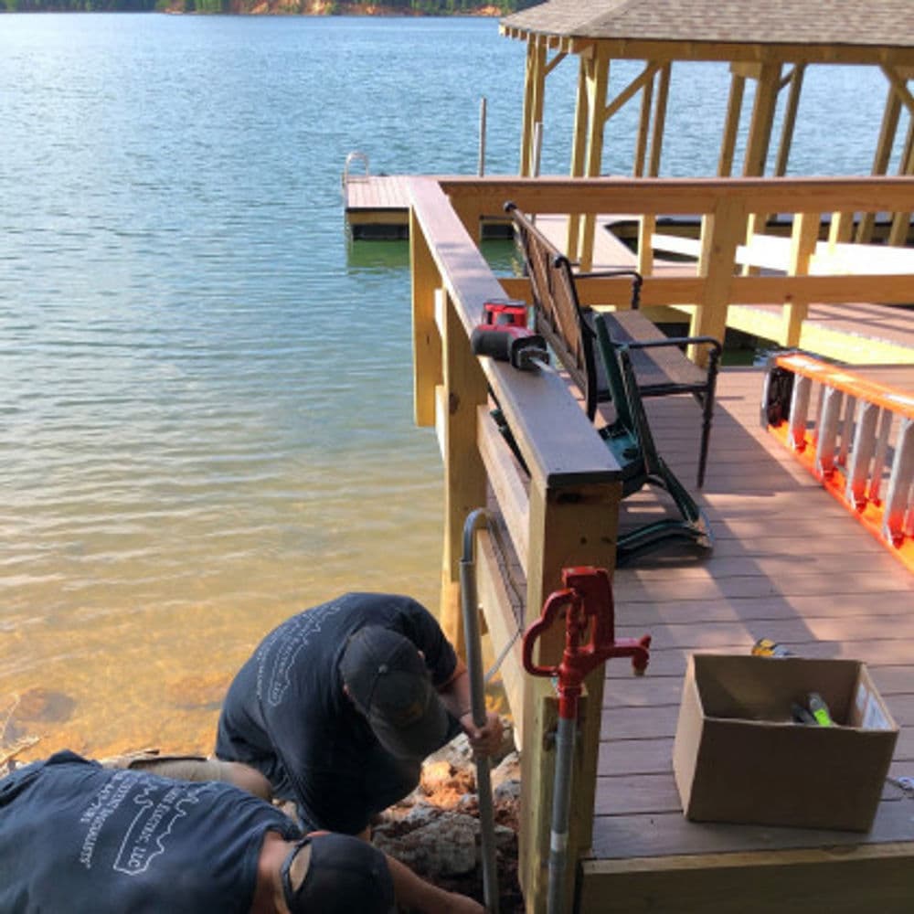 Workers installing a dock at a lakeside property with wooden structure and tools visible.